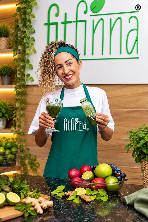 Zélia Gomes segurando uma taça de suco verde e uma garrafa Detox Power.